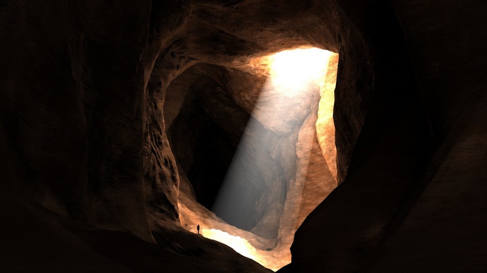 Silhouette in a dark cave with sun rays