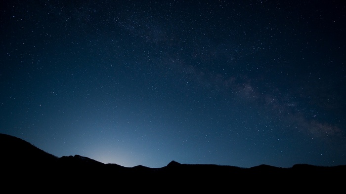 Night sky with stars and the Milky Way over a silhouette of mountains