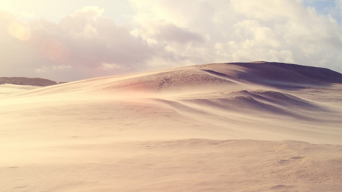 Sand dunes blowing in the wind under cloudy sky