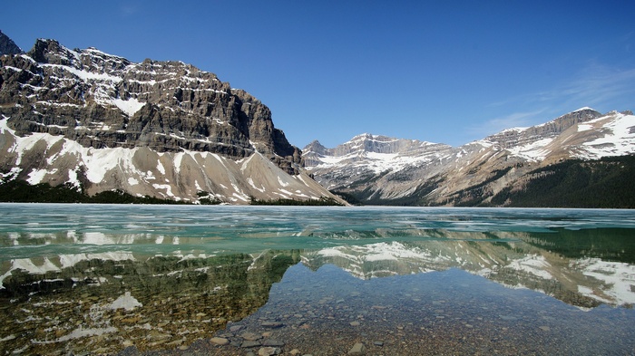 Snow-capped mountains reflected in a partially frozen lake