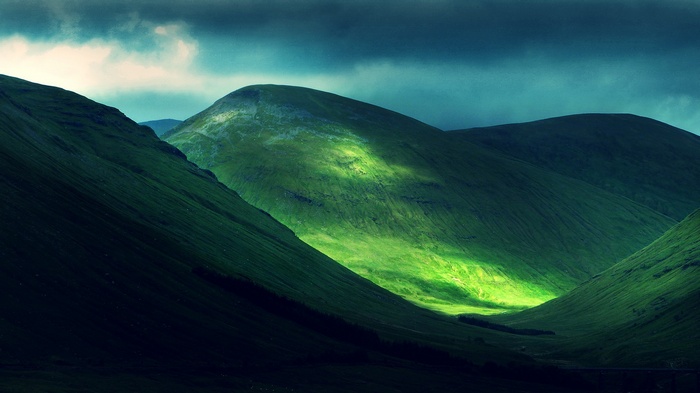 Sunlight illuminates green hills under a dark sky