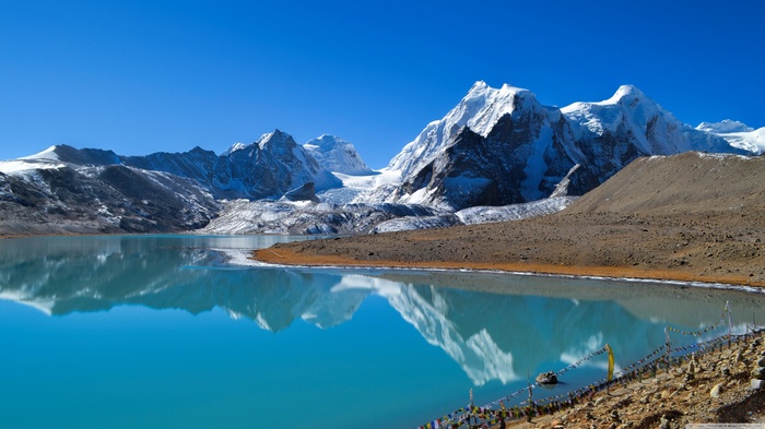 Turquoise lake reflecting snow-capped mountains under a clear blue sky