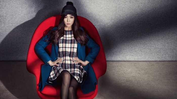 Tiffany Hwang sits in a red chair wearing a plaid dress and blue coat