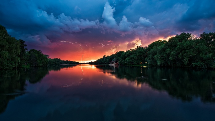 Lightning strikes over a lake at sunset with trees