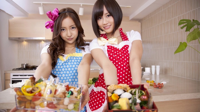 Two women holding bento boxes in a kitchen