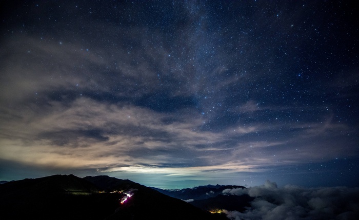 Night sky with stars over mountains and clouds