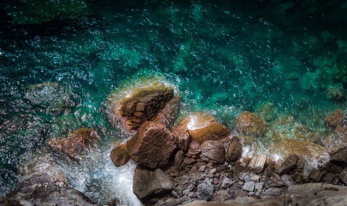 Aerial view of turquoise ocean waves crashing on rocky shore