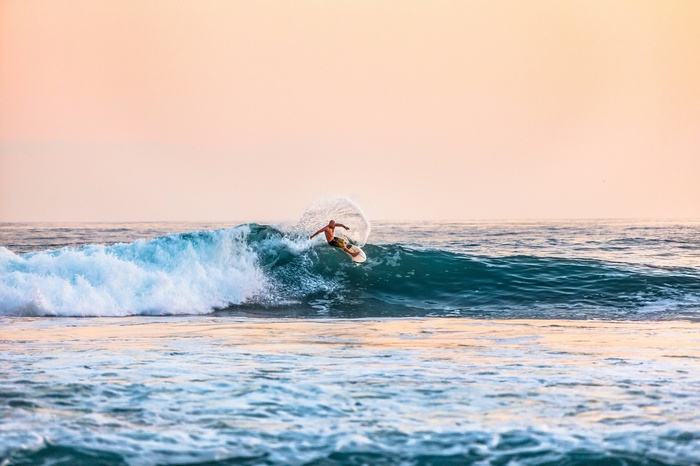 Surfer riding a wave in the ocean at sunset