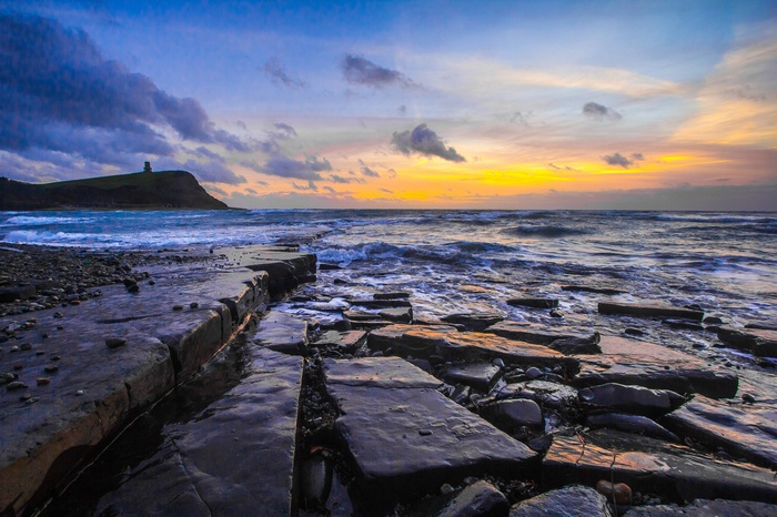 Sunset over the coast of Dorset with a tower on a hill