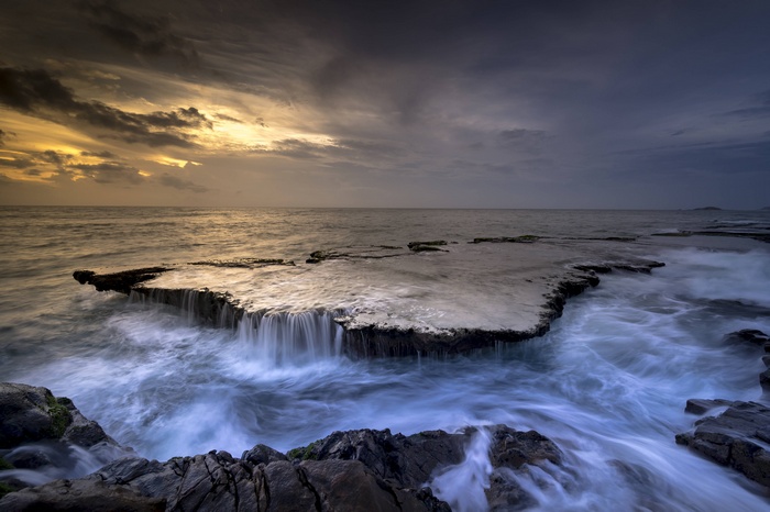 Ocean waves crashing on a rocky coast with a waterfall cascade