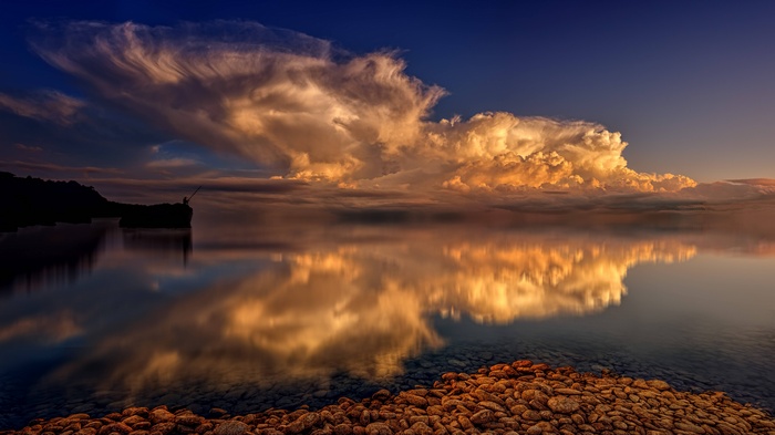 Fisherman on a rock with dramatic clouds over the sea