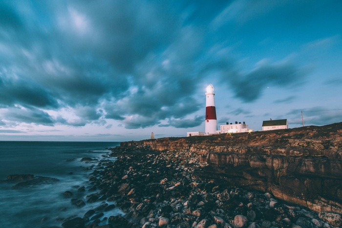 Red and white lighthouse on a rocky coast at dusk