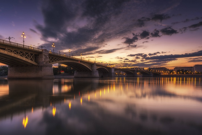 Bridge over river at dusk with city lights
