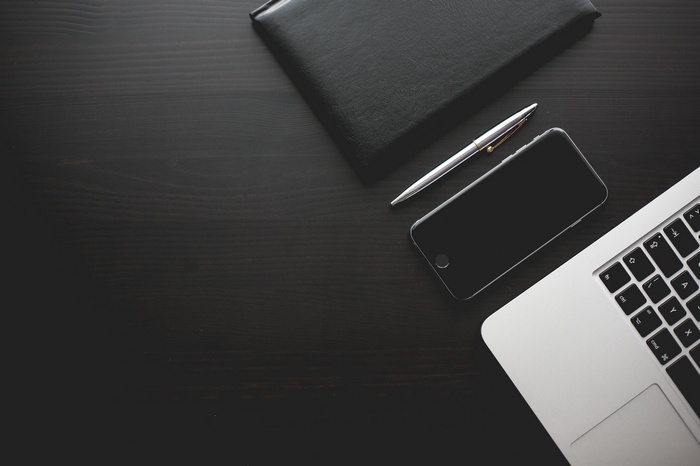 Black notebook, pen, smartphone, and laptop on a desk