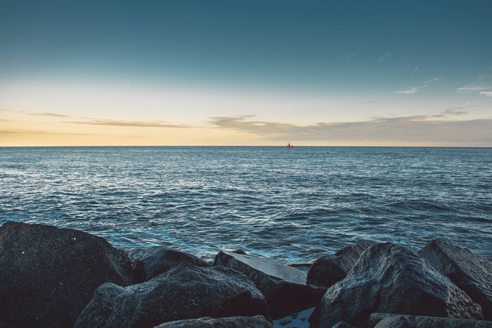 Sailboat on the horizon over the sea with rocks in the foreground