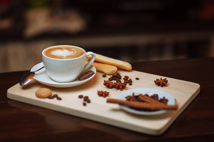 Cappuccino with coffee beans and spices on a wooden board