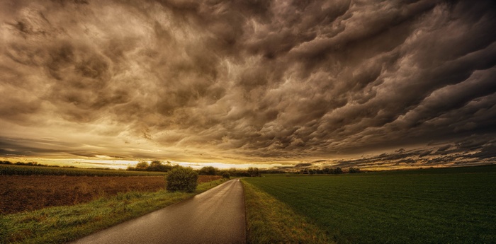 Panorama of a country road under stormy sunset clouds