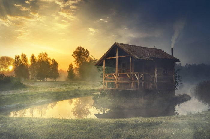 Wooden hut on a lake at sunrise with mist