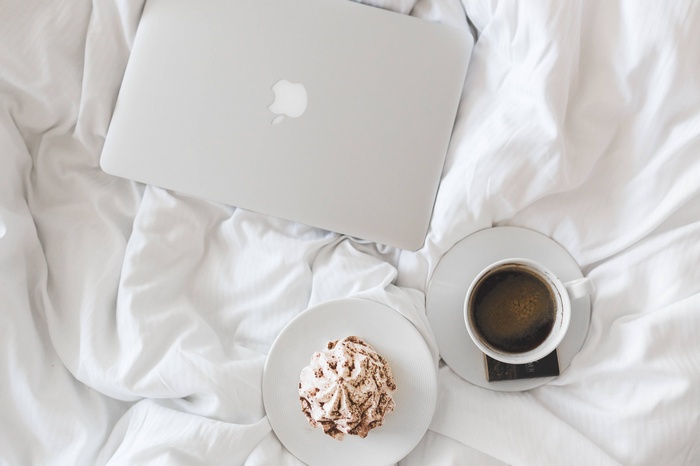 MacBook, coffee, and pastry on a white bed