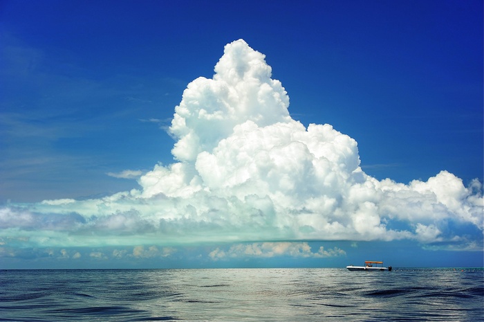 A boat on the ocean under a large cumulus cloud