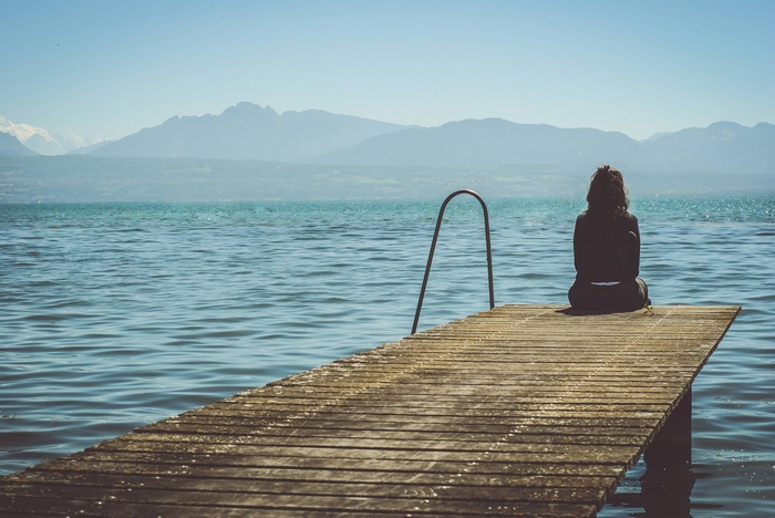 Woman sitting on a wooden pier overlooking a lake and mountains
