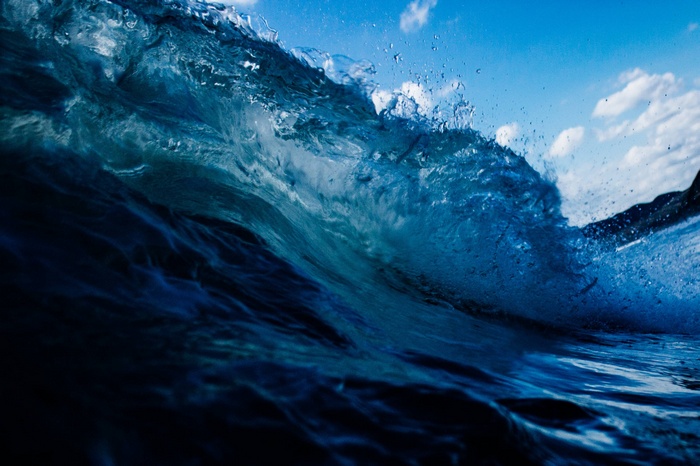 Blue ocean wave crashing under a cloudy sky