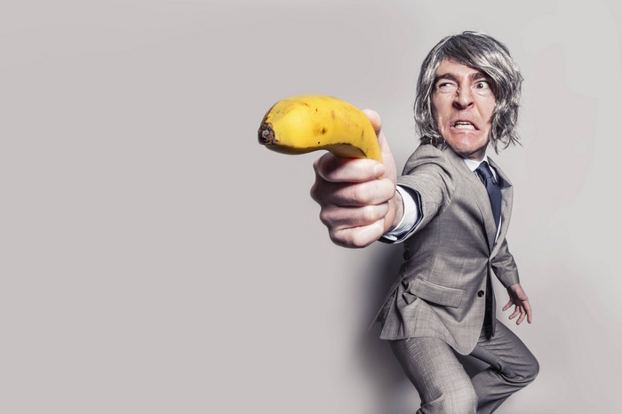 Man in suit holding a banana like a gun