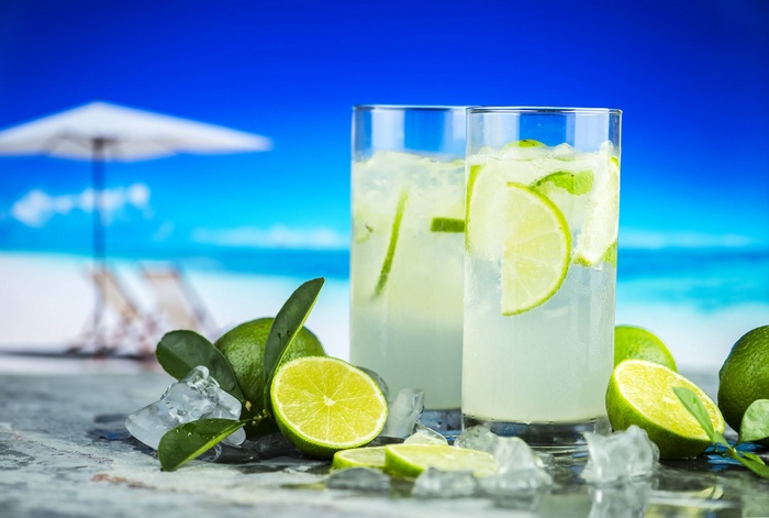 Two glasses of limeade with limes and ice on a beach background