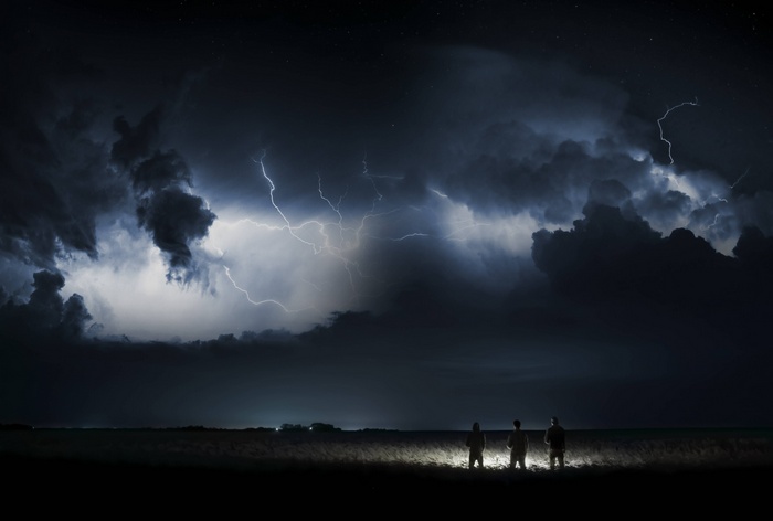Three people watch a powerful thunderstorm with lightning