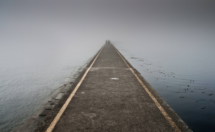 People walk on a foggy pier over the ocean at dawn