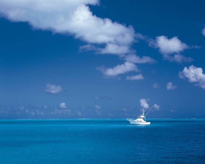 White boat on a bright blue ocean under a cloudy sky