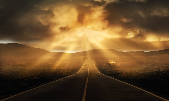A straight road through a landscape under dramatic clouds