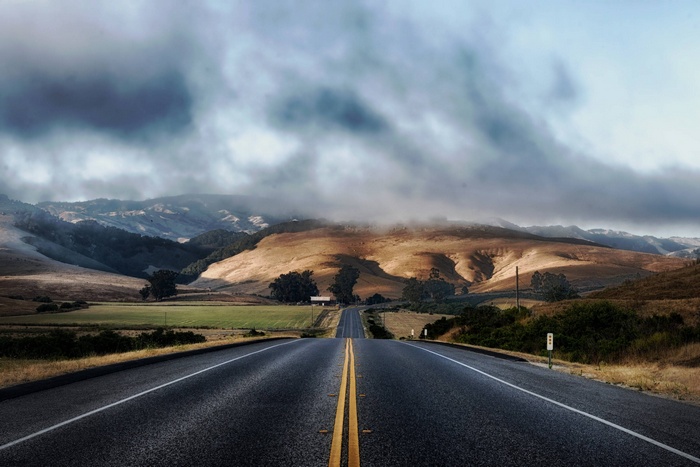 Road through rolling hills in California under cloudy skies