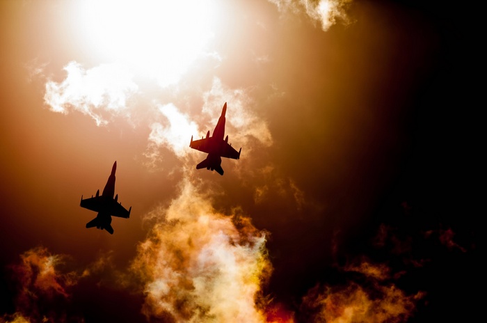 Two fighter jets flying through clouds at sunset