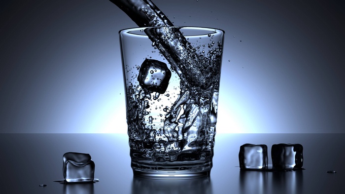 Water pouring into a glass with ice cubes