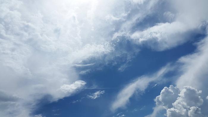 Blue sky with white clouds and a contrail