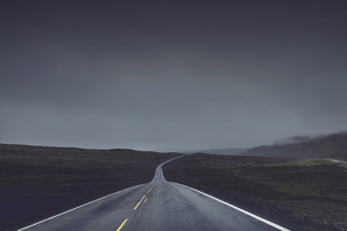 A lonely road through a dark, foggy landscape