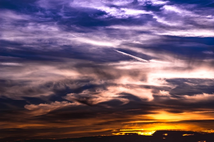 Dramatic sunset sky with colorful clouds and contrail
