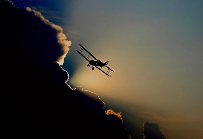 Biplane flying through clouds at sunset