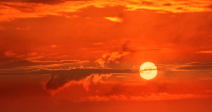 The sun setting behind clouds in a vibrant orange sky.