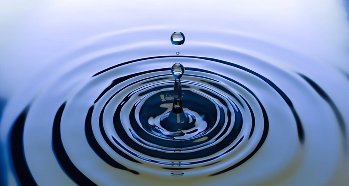 Water drop creating ripples on a blue surface