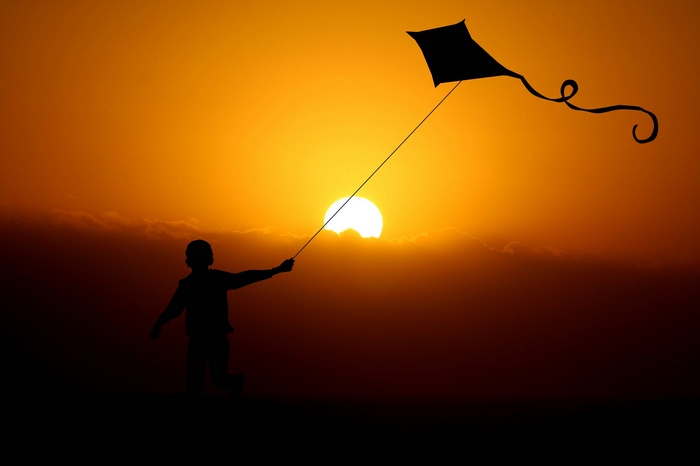 Silhouette of a boy flying a kite at sunset