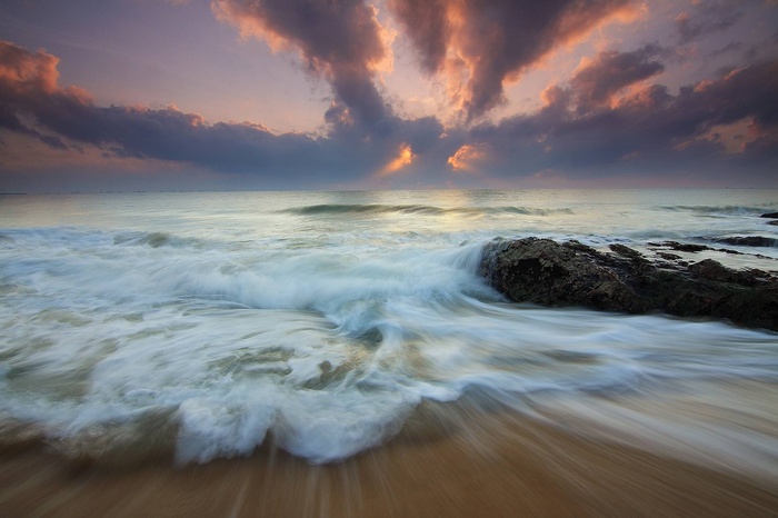 Sunrise over the ocean with waves crashing on rocks