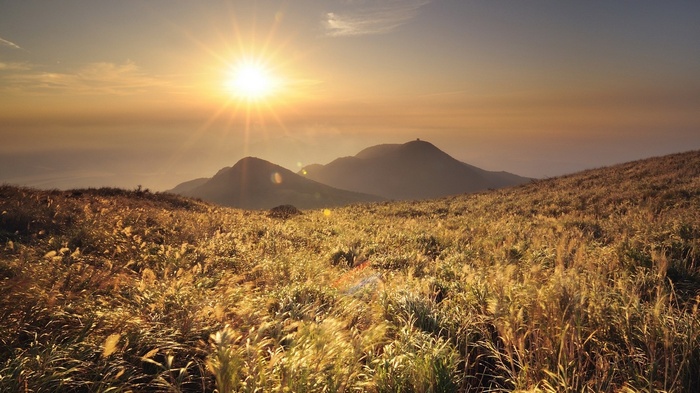 Golden sun over grassy mountains at sunset