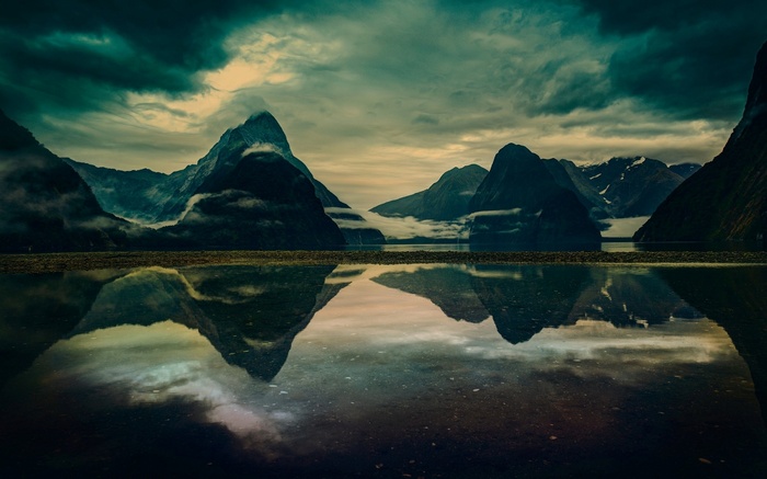 Mountain range reflected in still water under cloudy sky
