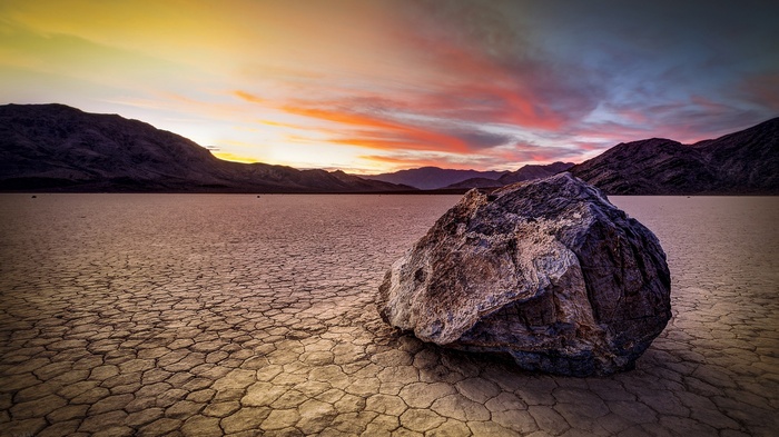 Rock on cracked desert floor at sunset