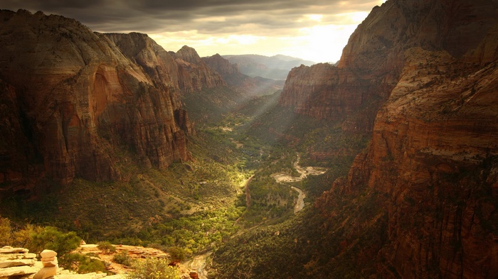 Sunlight streams into a deep canyon with a winding river.