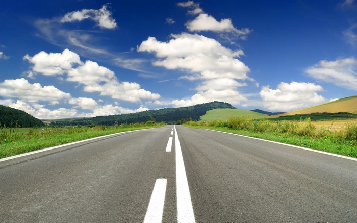 Empty road through rolling hills under a blue sky