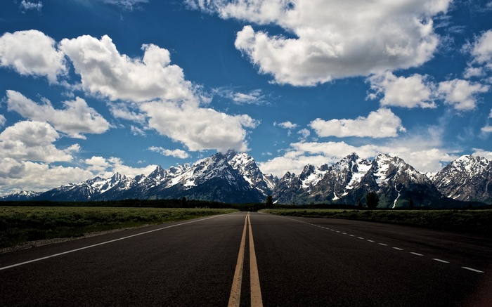 Road leading to snow-capped mountains under a cloudy sky