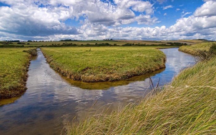A winding river through green fields under a cloudy sky